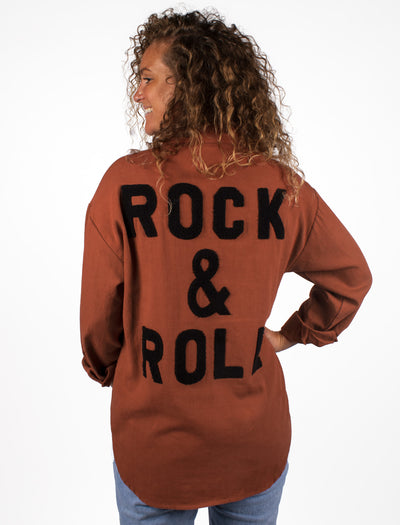 Roestbruine blouse met badstof artwork op de achterzijde: ROCK & ROLL! De blouse heeft een tone in tone knoopsluiting. Doordat de blouse een mooie lengte heeft, is hij zowel over de broek als gebloused in de broek te dragen. De blouse schijnt niet door. 